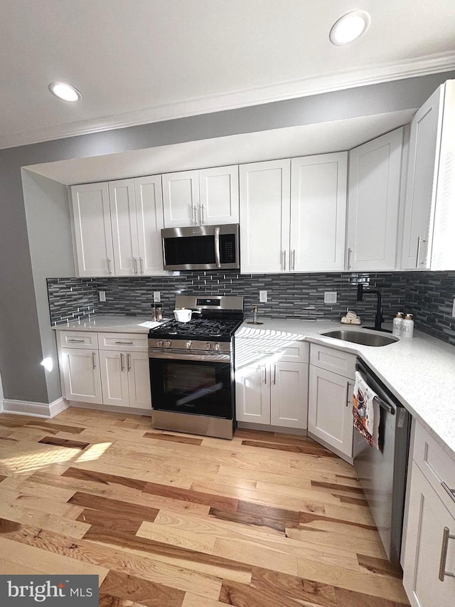 kitchen featuring light wood-type flooring, backsplash, stainless steel appliances, sink, and white cabinets