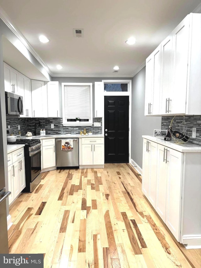 kitchen with white cabinetry, ornamental molding, light wood-type flooring, and appliances with stainless steel finishes