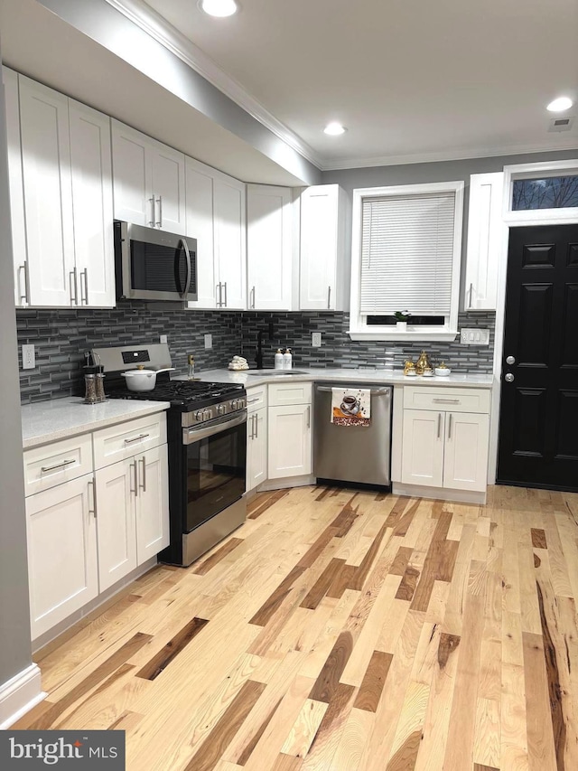 kitchen with white cabinets, appliances with stainless steel finishes, backsplash, and light hardwood / wood-style flooring