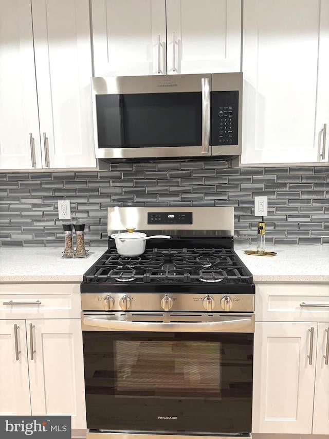 kitchen with white cabinetry, light stone countertops, appliances with stainless steel finishes, and tasteful backsplash