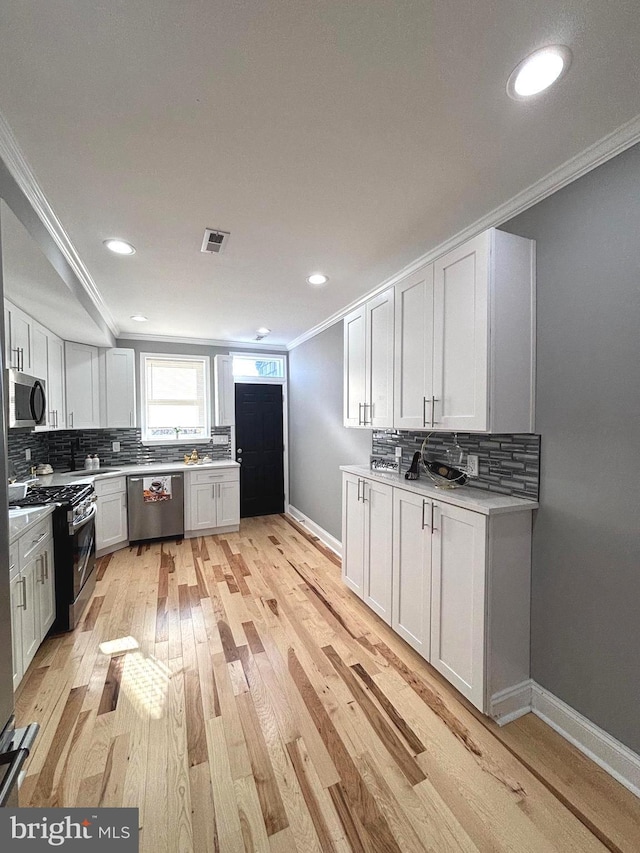 kitchen featuring white cabinets, ornamental molding, appliances with stainless steel finishes, tasteful backsplash, and light hardwood / wood-style floors