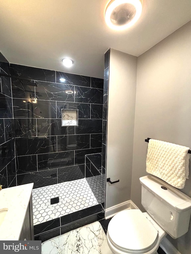 bathroom with a tile shower, vanity, and toilet