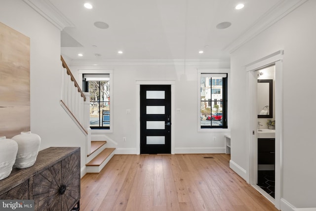 entrance foyer with ornamental molding, a wealth of natural light, stairway, and light wood-style flooring