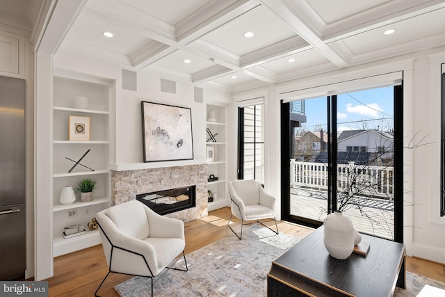 living area featuring light wood-type flooring, coffered ceiling, beam ceiling, and a glass covered fireplace