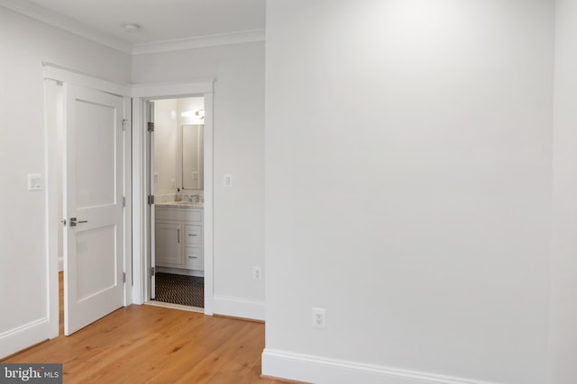 unfurnished bedroom featuring baseboards, connected bathroom, wood finished floors, crown molding, and a sink