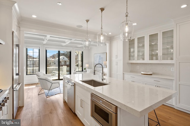 kitchen featuring a kitchen island with sink, stainless steel appliances, a sink, white cabinetry, and glass insert cabinets