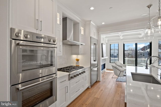 kitchen featuring wall chimney exhaust hood, appliances with stainless steel finishes, hanging light fixtures, white cabinetry, and a sink