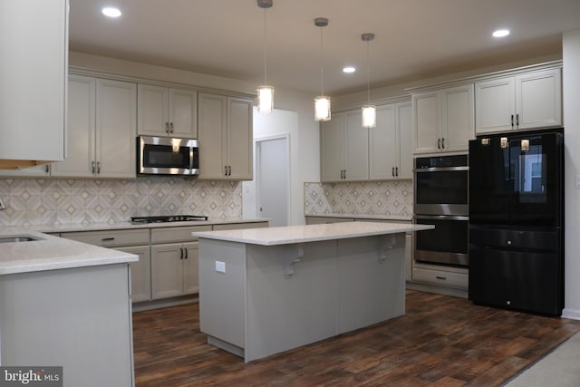 kitchen featuring dark hardwood / wood-style floors, pendant lighting, decorative backsplash, a kitchen island, and appliances with stainless steel finishes