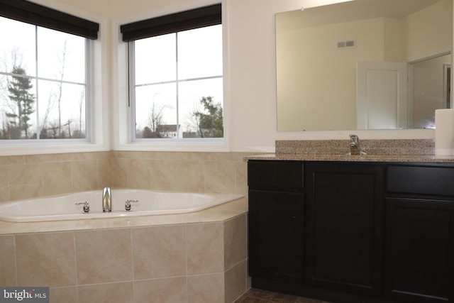 bathroom featuring vanity, a relaxing tiled tub, and a wealth of natural light