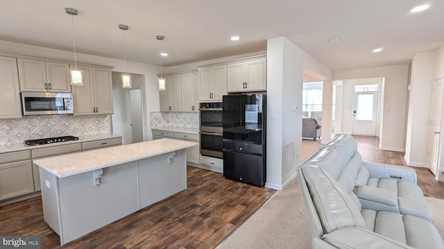 kitchen featuring hanging light fixtures, decorative backsplash, gray cabinets, appliances with stainless steel finishes, and a kitchen bar