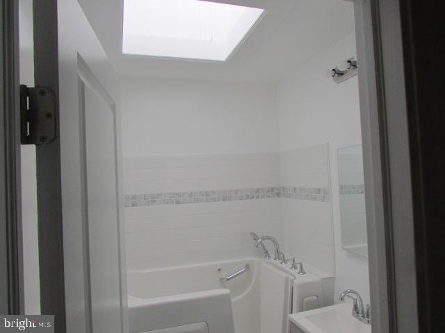 bathroom featuring a tub to relax in, a skylight, and sink