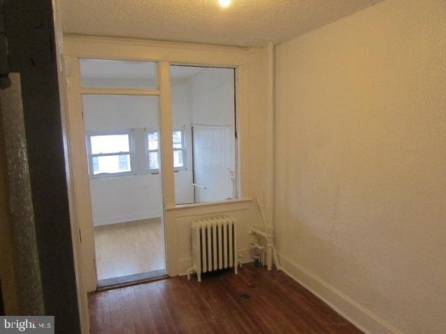 unfurnished room featuring radiator heating unit, a textured ceiling, and dark wood-type flooring