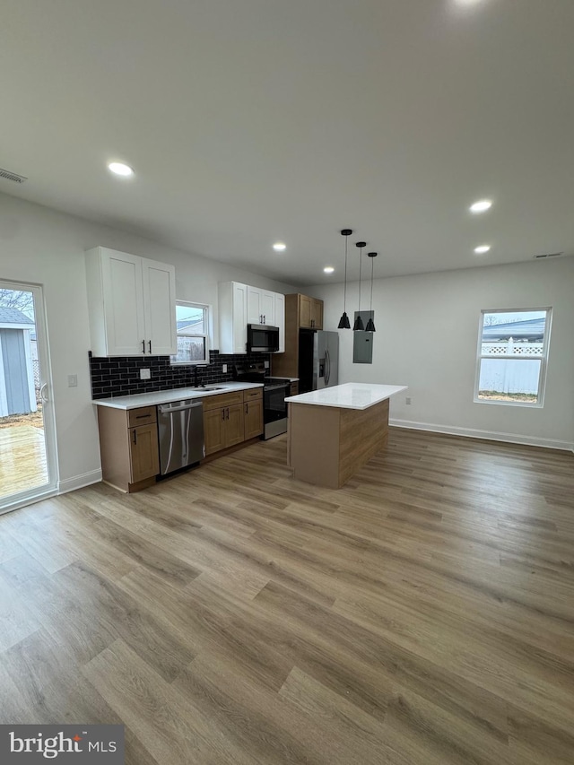 kitchen with stainless steel appliances, decorative light fixtures, a center island, light hardwood / wood-style floors, and white cabinetry