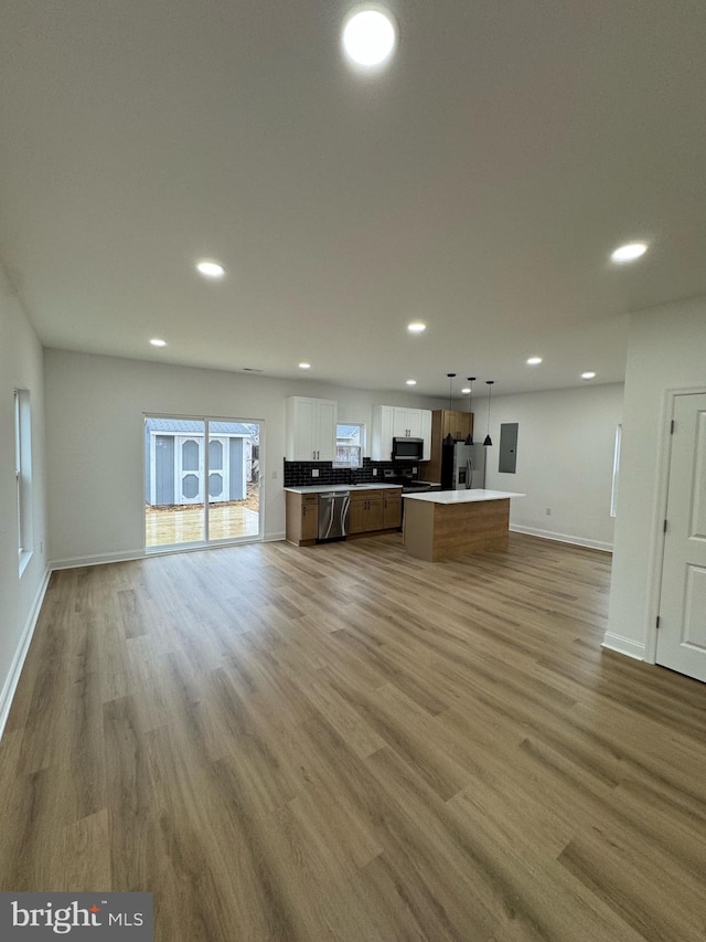 kitchen with stainless steel appliances, a kitchen island, decorative light fixtures, hardwood / wood-style floors, and white cabinetry