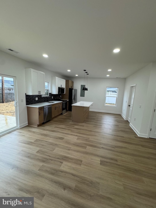 kitchen with appliances with stainless steel finishes, pendant lighting, a center island, light hardwood / wood-style floors, and white cabinetry