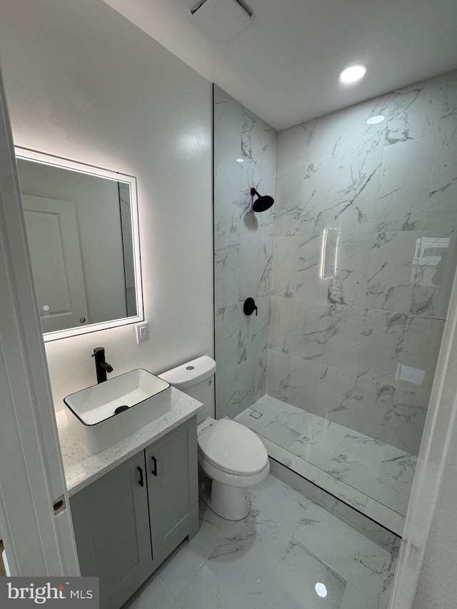 bathroom with a tile shower, vanity, and toilet