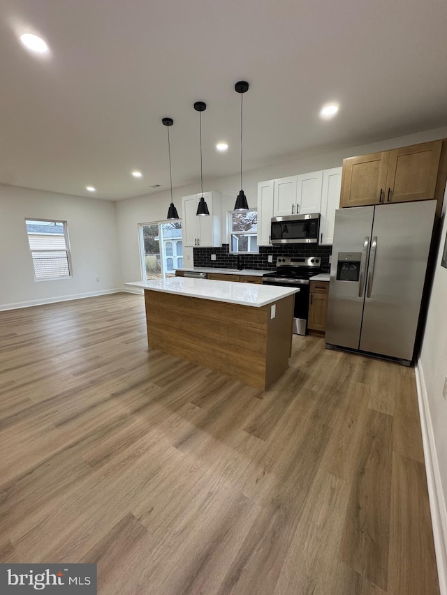 kitchen featuring white cabinetry, stainless steel appliances, pendant lighting, a kitchen island, and light wood-type flooring