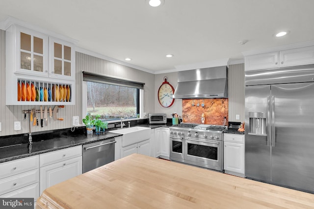 kitchen featuring premium appliances, crown molding, sink, wall chimney range hood, and white cabinets