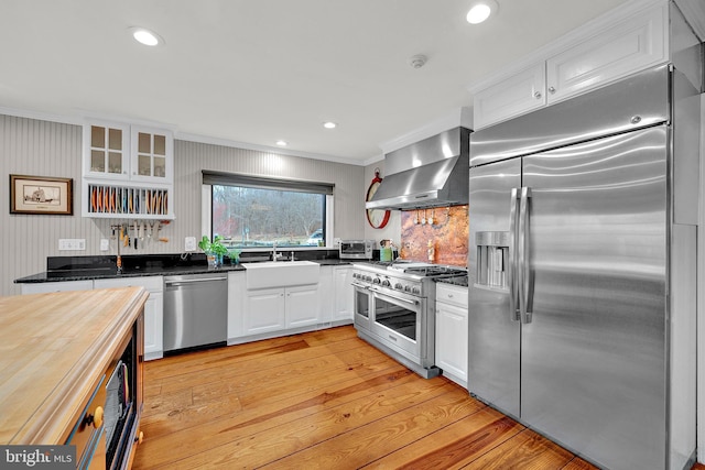 kitchen featuring ornamental molding, premium appliances, sink, wall chimney range hood, and white cabinetry