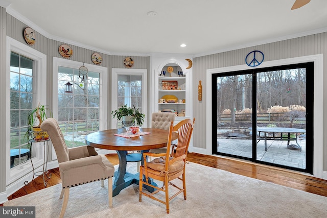 dining space featuring hardwood / wood-style floors, built in features, ornamental molding, and a wealth of natural light