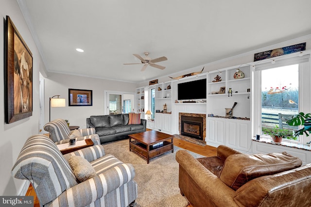 carpeted living room featuring built in shelves, ceiling fan, a fireplace, and ornamental molding