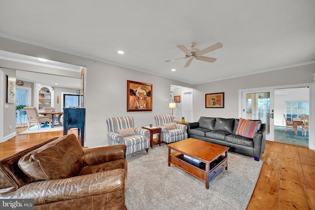 living room with built in shelves, ceiling fan, hardwood / wood-style floors, and ornamental molding