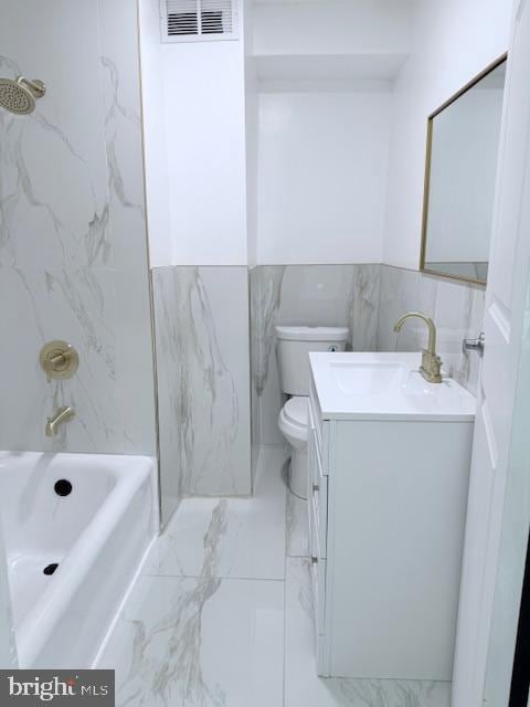 full bathroom with vanity, toilet, tiled shower / bath, and tile walls