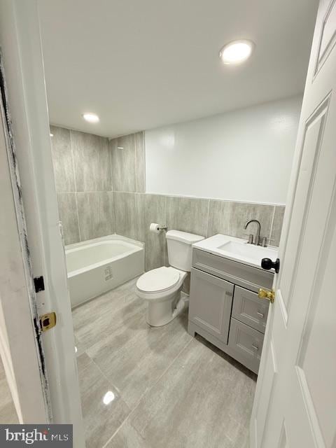 bathroom featuring a bathtub, vanity, tile walls, and toilet