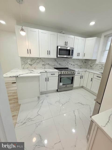 kitchen with light stone countertops, kitchen peninsula, pendant lighting, white cabinets, and appliances with stainless steel finishes