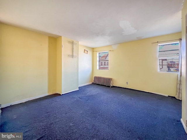 unfurnished room with dark colored carpet and radiator heating unit