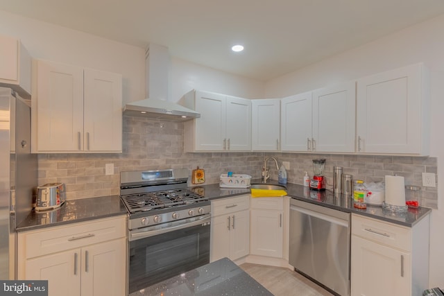 kitchen featuring appliances with stainless steel finishes, sink, white cabinetry, and wall chimney range hood