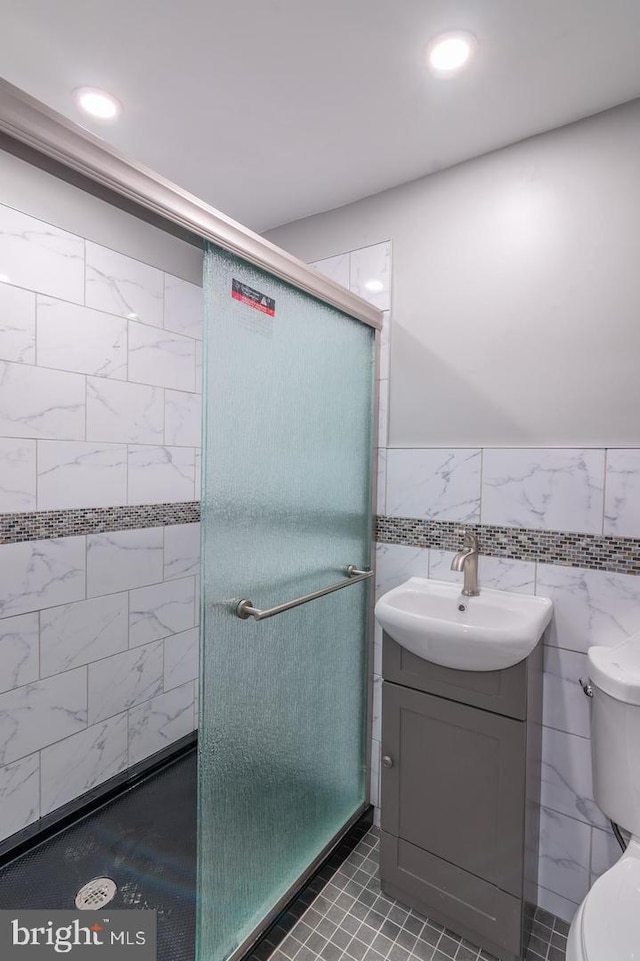 bathroom with vanity, a shower with door, tile patterned flooring, toilet, and tile walls