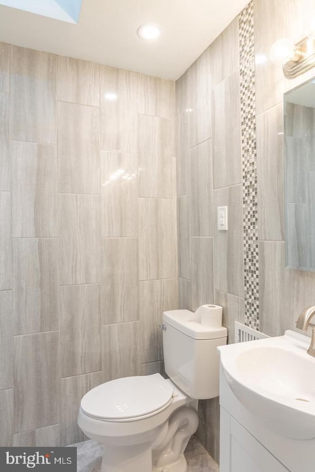 bathroom featuring vanity, toilet, and tile walls