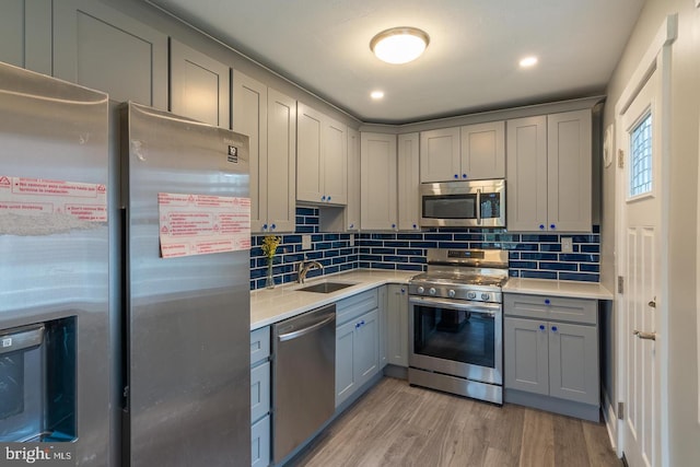 kitchen featuring sink, decorative backsplash, gray cabinets, light wood-type flooring, and appliances with stainless steel finishes