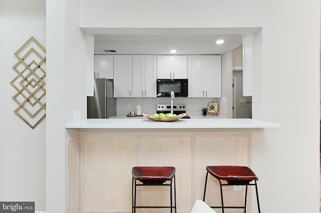 5284 Davis Ford Rd, Woodbridge, VA 22192 - kitchen featuring black microwave, freestanding refrigerator, electric range oven, a breakfast bar area, and backsplash