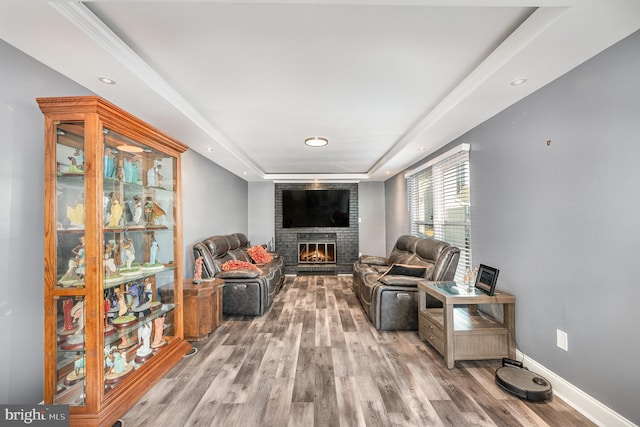 living area featuring a raised ceiling, a brick fireplace, and light wood-type flooring