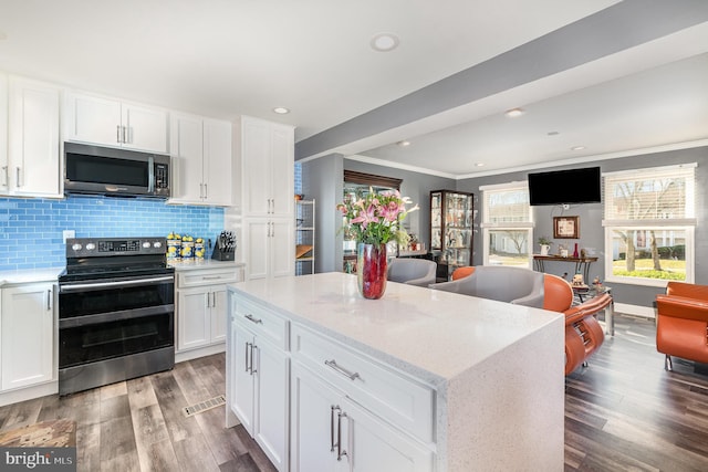 kitchen featuring hardwood / wood-style floors, white cabinets, backsplash, a center island, and stainless steel appliances