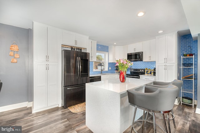 kitchen with sink, a kitchen breakfast bar, a center island, black appliances, and white cabinets