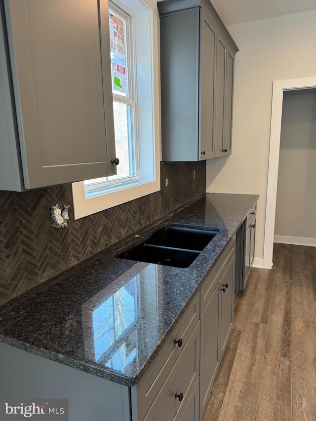 kitchen featuring baseboards, dark stone counters, decorative backsplash, wood finished floors, and gray cabinets