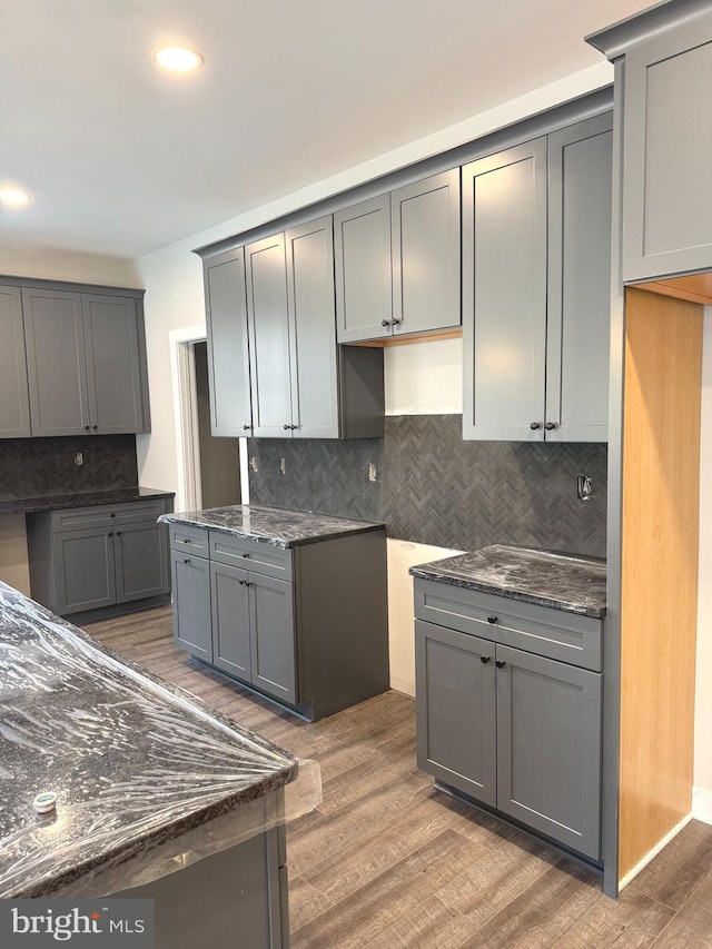 kitchen featuring gray cabinets, dark stone countertops, and wood finished floors