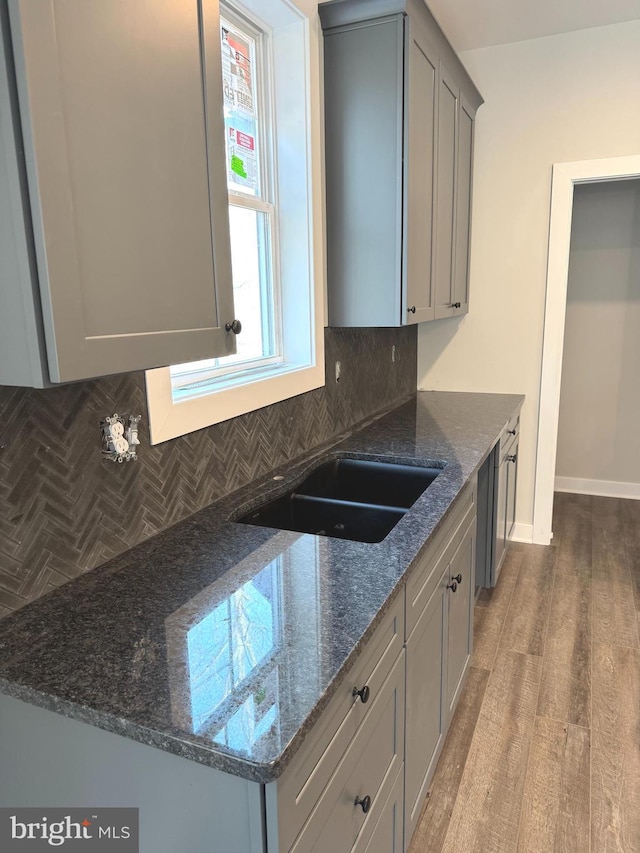 kitchen with dark stone countertops, gray cabinets, decorative backsplash, and wood finished floors