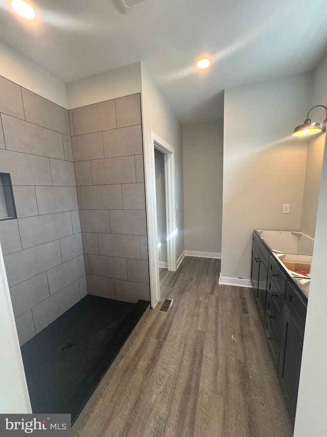 bathroom featuring double vanity, visible vents, wood finished floors, tiled shower, and baseboards