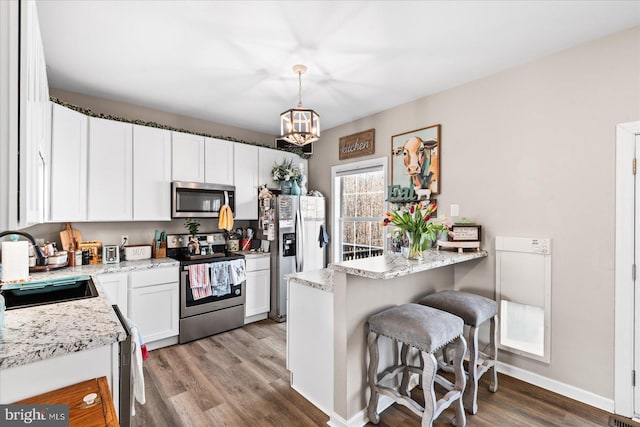 kitchen with sink, appliances with stainless steel finishes, light stone counters, white cabinets, and decorative light fixtures