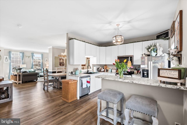 kitchen with sink, white cabinetry, stainless steel appliances, light stone countertops, and decorative light fixtures