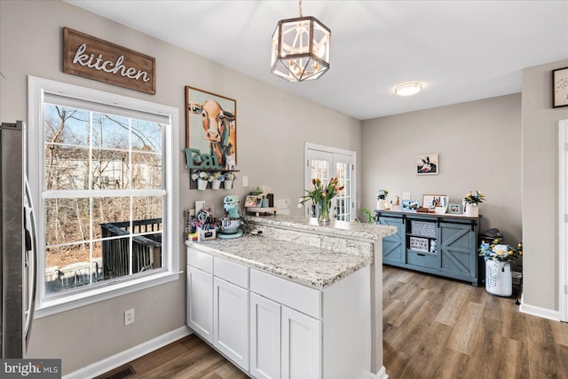 kitchen featuring stainless steel refrigerator, decorative light fixtures, white cabinets, hardwood / wood-style flooring, and kitchen peninsula