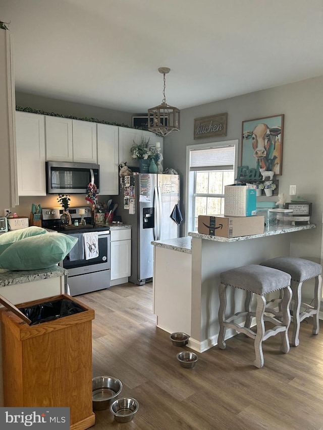 kitchen featuring appliances with stainless steel finishes, white cabinetry, light stone counters, light hardwood / wood-style floors, and decorative light fixtures