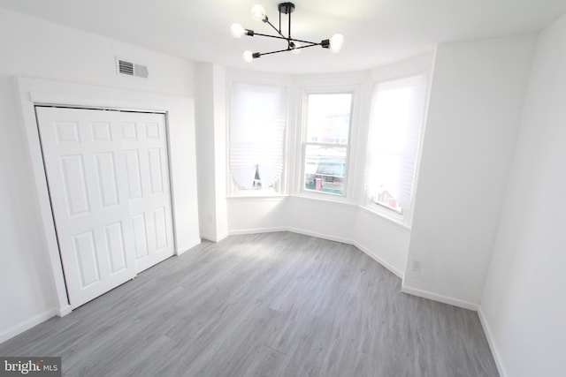 unfurnished bedroom featuring a chandelier, light hardwood / wood-style floors, and a closet