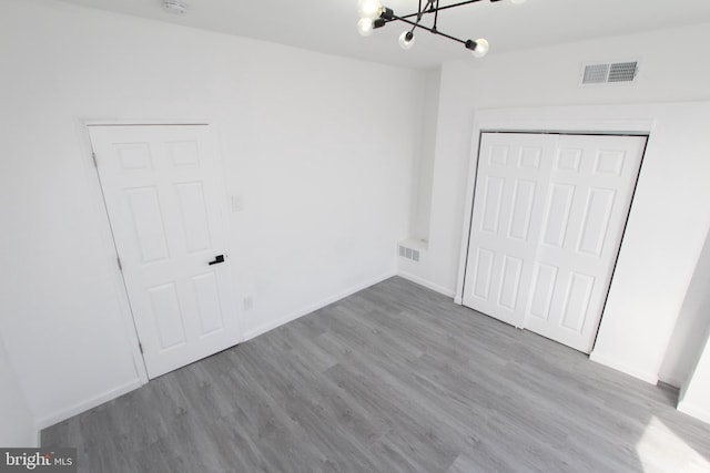 unfurnished bedroom featuring a notable chandelier, light hardwood / wood-style flooring, and a closet