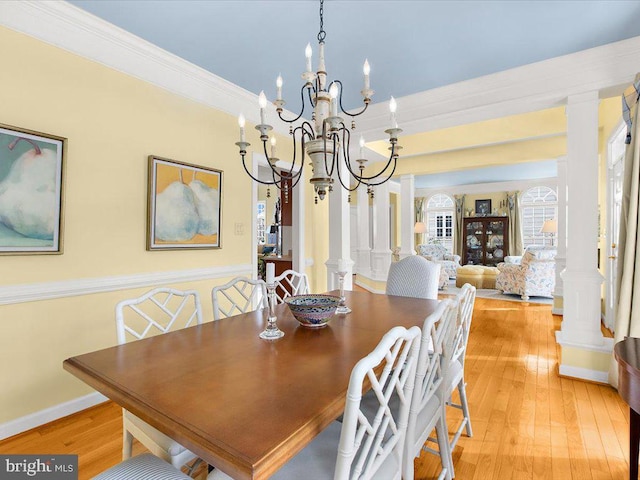 dining space featuring crown molding, a notable chandelier, light hardwood / wood-style flooring, and ornate columns