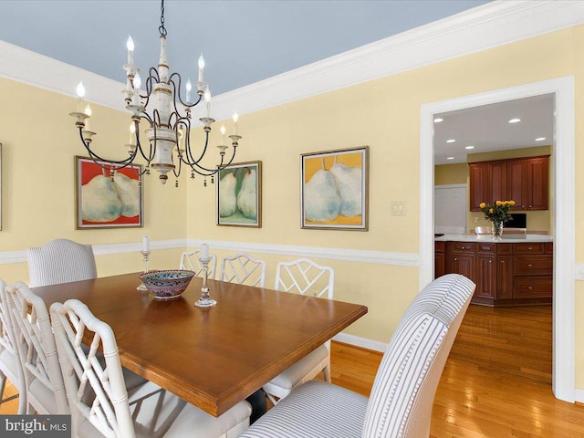 dining area featuring light wood-type flooring, ornamental molding, and an inviting chandelier